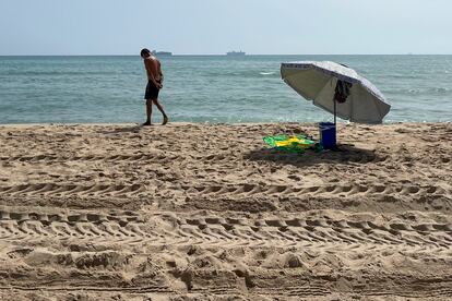 Una persona pasea por una de las tres playas del sur de València afectadas desde el martes por un vertido de hidrocarburos que han reabierto este jueves el acceso al público, pero lo han hecho con bandera roja, que prohíbe el baño.