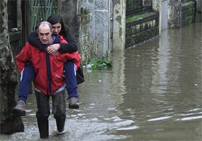 Un hombre con botas de agua traslada a una joven por la inundada carretera GI-131, a su paso  el barrio donostiarra de Martutene.