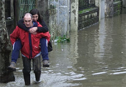 Un hombre con botas de agua traslada a una joven por la inundada carretera GI-131, a su paso  el barrio donostiarra de Martutene.