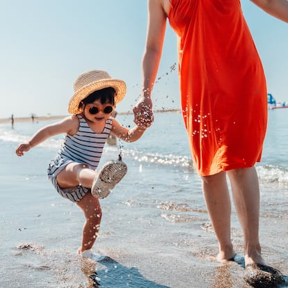 Cropped shot of mother and her little girl walking on the beach against blue sky on a sunny day. Summer family vacation. Motherhood and wellbeing concept.