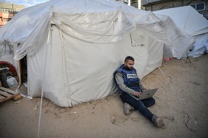 Un periodista sentado junto a una tienda de campaña mientras intenta conectarse a internet en Rafah, Gaza