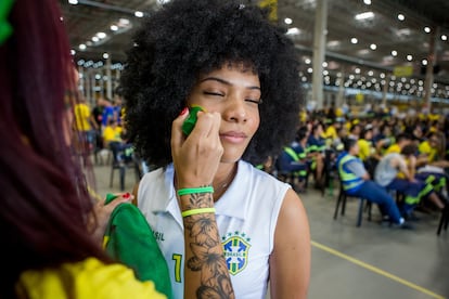 A woman paints the face of another to support the team. 