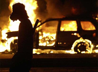 Un manifestante pasa ayer junto a un vehículo incendiado durante los disturbios en Oaxaca.