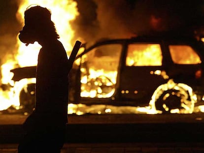 Un manifestante pasa ayer junto a un vehículo incendiado durante los disturbios en Oaxaca.