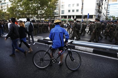 La lluvia intermitente ha provocado que muchas autoridades, entre ellas los presidentes autonómicos de Madrid, Ángel Garrido; Castilla y León, Juan Vicente Herrera; y Cantabria, Miguel Ángel Revilla, recurrieran a un impermeable transparente para protegerse, al igual que ha hecho Manuela Carmena. En la imagen, un ciclista contempla a los militares momentos antes del acto.