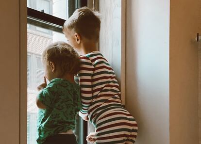 Dos hermanos miran por la ventana de su cuarto.