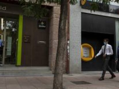 Varias personas caminan al lado de una oficina de Bankia y otra de CaixaBank.