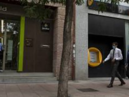 Varias personas caminan al lado de una oficina de Bankia y otra de CaixaBank.