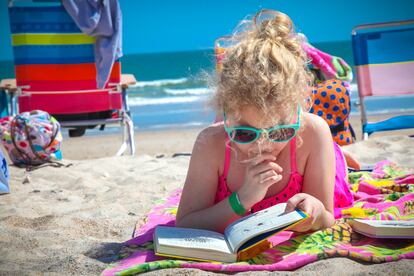 Una niña lee en la playa.