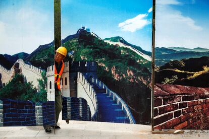 Un trabajador mira a través de una valla de una obra de construcción decorada con imágenes de la Gran Muralla en Badaling (China).