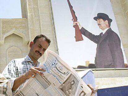 Un iraquí lee el diario <b><i>Iraq,</b></i> ayer, ante un retrato gigante de Sadam Husein.