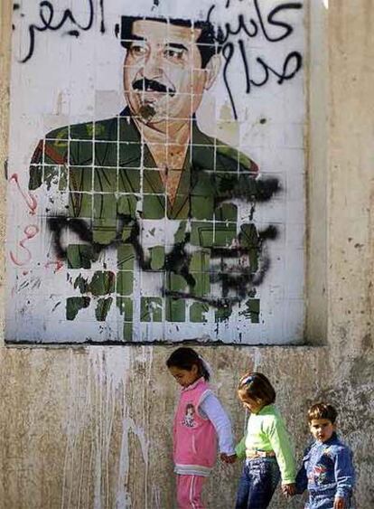 Unos niños pasan junto a un mural destrozado con la cara de Sadam Husein en su aldea natal, Tikrit.