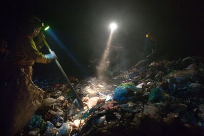 Las linternas de varias personas iluminan la basura en el vertedero de Siem Reap, mientras buscan algún objeto que recuperar.