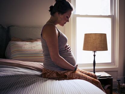 Una mujer embarazada sentada su cama.