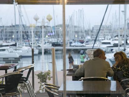 Una pareja en la terraza de una cafetería con vistas al puerto de Alicante.