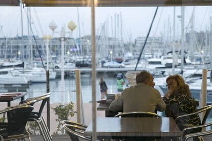 Una pareja en la terraza de una cafetería con vistas al puerto de Alicante.