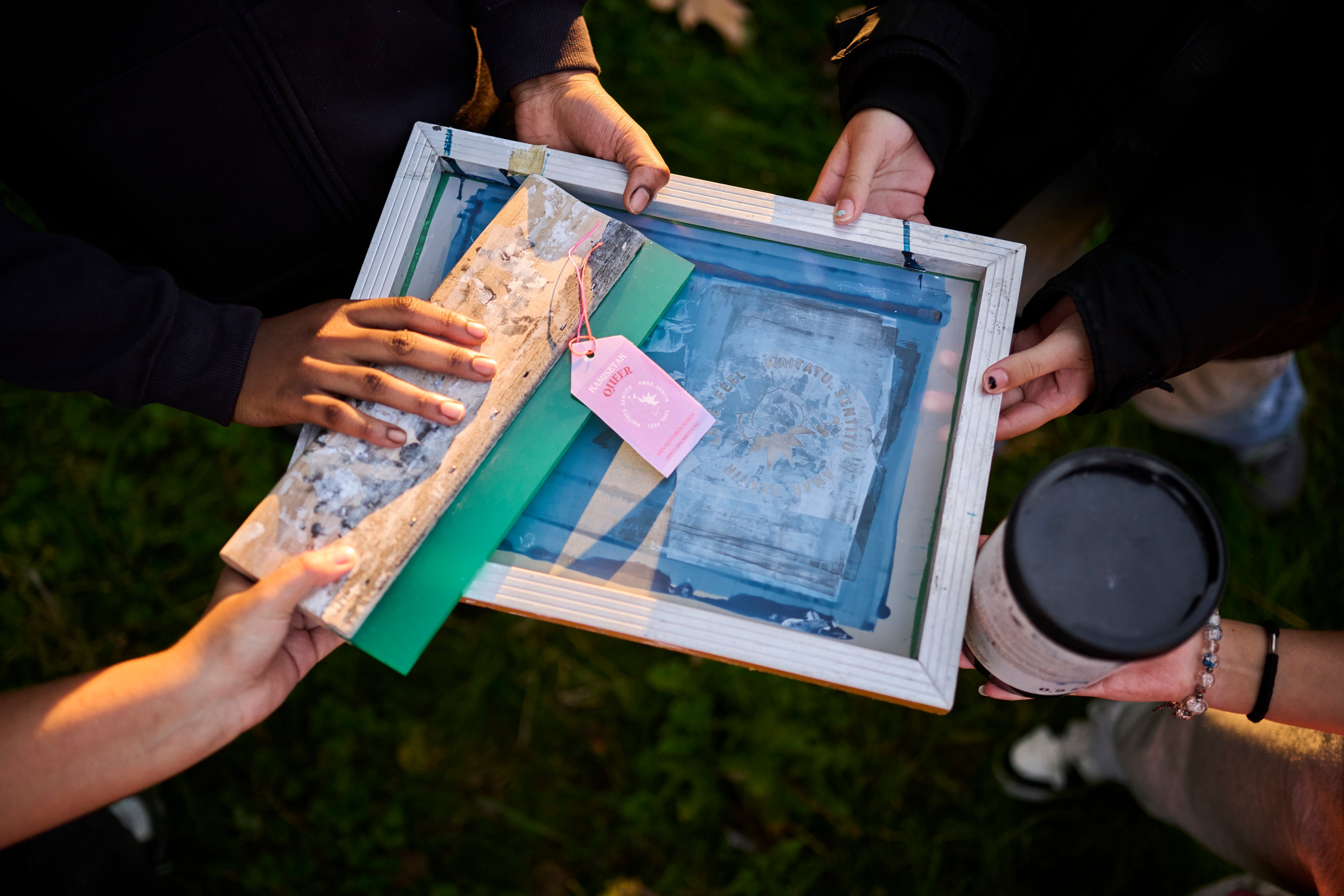 Varias personas sostienen las herramientas para hacer las camisetas para la caja de resistencia LGTBIQI+.