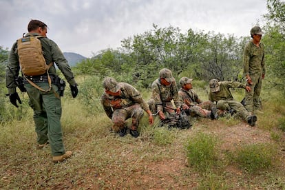 Cinco migrantes con vestimenta de camuflaje son esposados luego de ser aprehendidos por agentes de la Patrulla Fronteriza.