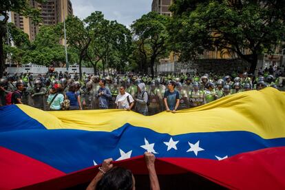 Um grupo de manifestantes agita uma bandeira da Venezuela diante de membros da Polícia Nacional Bolivariana.