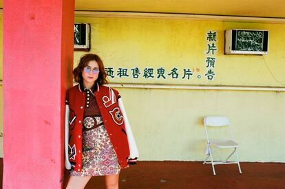 Russian Red en el Chinatown de Los Ángeles con minivestido y bomber oversize de Coach. Las gafas son el modelo Round Metal de Ray-Ban. El tono unificado y luminoso de su piel se consigue con el fondo de maquillaje Touche Éclat Le Teint de YSL Beauté.