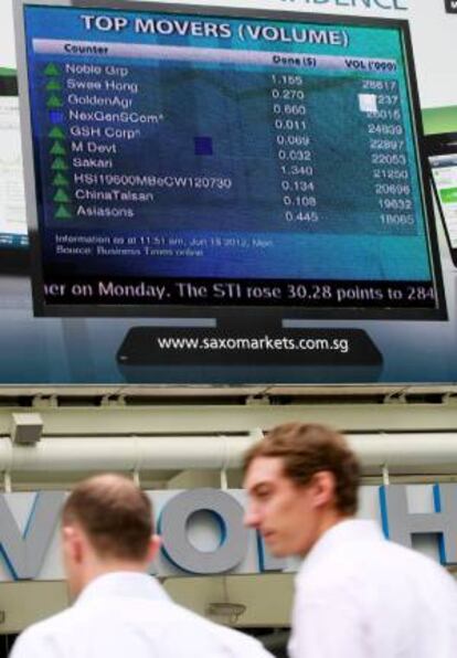 Dos hombres caminan junto a una pantalla que muestra la información de la bolsa en Singapur. EFE/Archivo