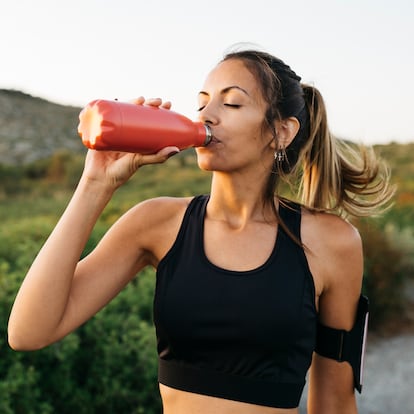 Fit young Woman in black sportswear drinking water from a reusable metal bottle after running workout