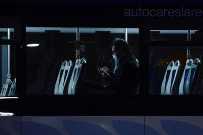 Un hombre observa su teléfono móvil en el interior de un autobús, camino a su puesto de trabajo, en la ciudad de Valladolid.