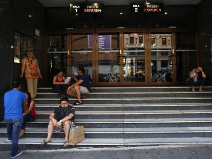 Varias personas descansan en las escaleras de un cine en la Gran Vía, en Madrid.
