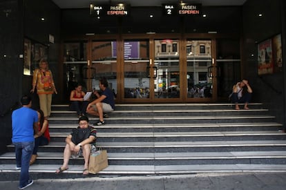 Varias personas descansan en las escaleras de un cine en la Gran Vía, en Madrid.