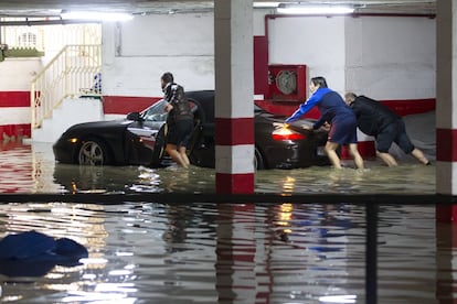 Varias personas empujan un vehículo en un garaje anegado por las fuertes lluvias caídas esta noche en la capital malagueña.