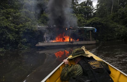 Agente do Ibama observa um barco de mineração incendiado nas margens do rio Uraricoera.