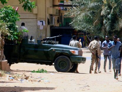 Un grupo de gente pasa delante de un vehículo militar en Jartum (Sudán), este sábado.