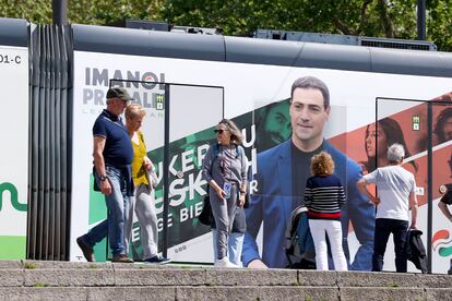Ciudadanos pasan por delante de un tranvía con publicidad del candidato del PNV, Imanol Pradales.