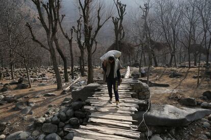 Un hombre cruza un puente de madera mientras transporta un saco de arroz en Kokernag, en la región de Cachemira (India).