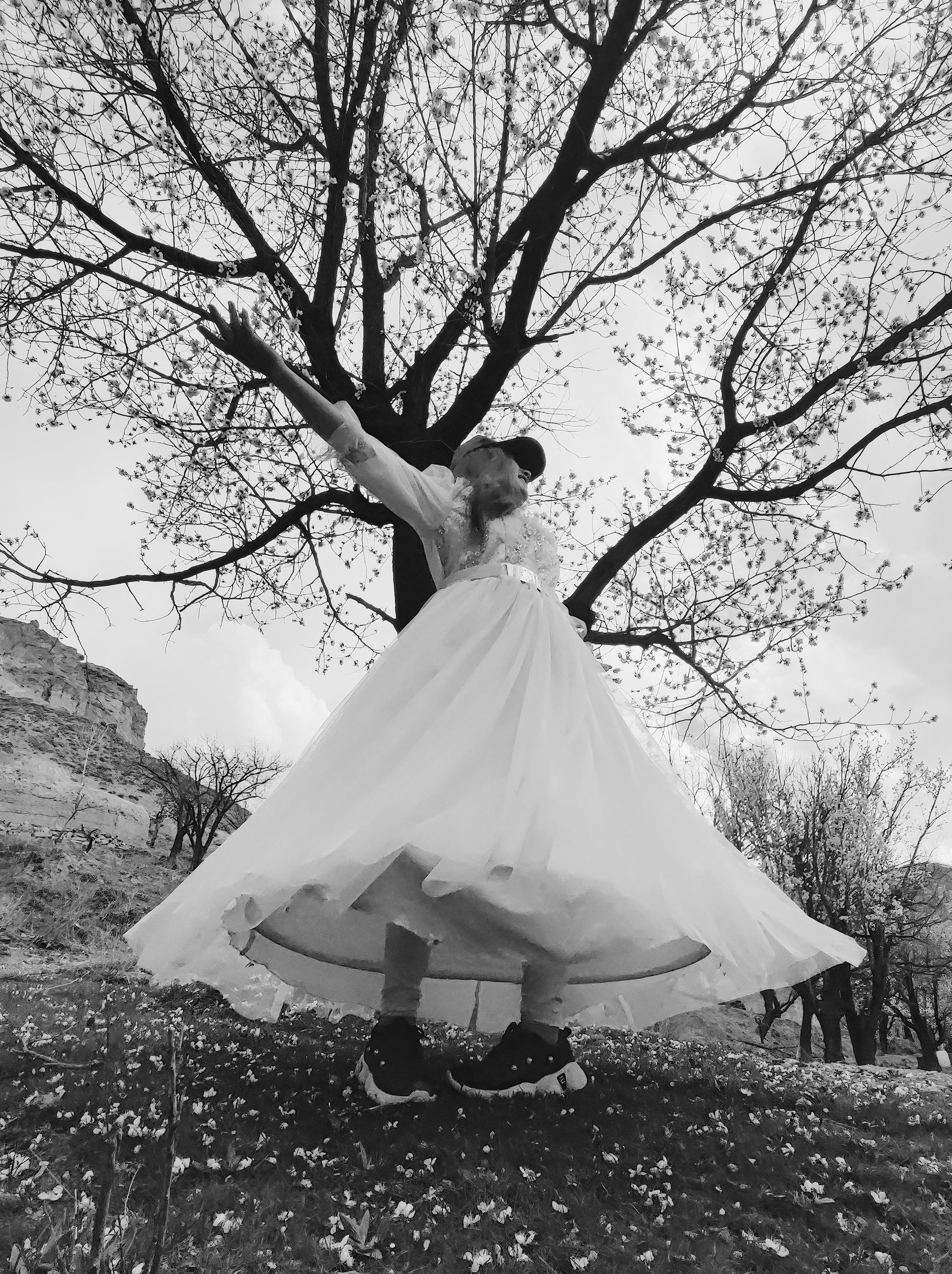 Una joven afgana vestida de novia, pero con zapatillas deportivas y visera, abre los brazos, rodeada de naturaleza.