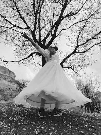 Una joven afgana vestida de novia, pero con zapatillas deportivas y visera, abre los brazos, rodeada de naturaleza.