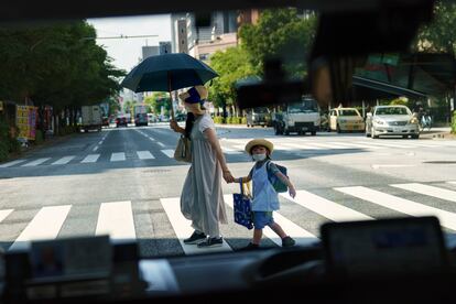 A pedestrian crossing a street with a child is seen through a taxi window in Tokyo, Monday, July 19, 2021