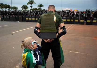 Un partidario del expresidente de extrema derecha de Brasil, Jair Bolsonaro, protege a una mujer arrodillada durante las protestas.