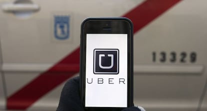 La pantalla de un m&oacute;vil con el logo de Uber frente a un taxi de Madrid. 