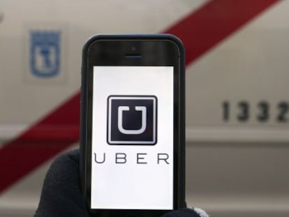 La pantalla de un m&oacute;vil con el logo de Uber frente a un taxi de Madrid. 