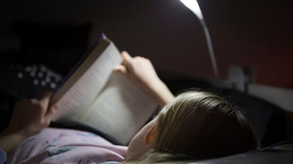 Joven de espaldas leyendo en la cama por la noche con una lámpara de lectura.