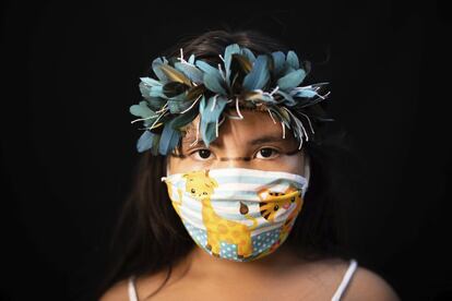 Iasmin, de ocho años, del grupo étnico indígena sateré mawé, posa para un retrato con el tocado tradicional de su tribu y una máscara facial de motivos infantiles, en Manaos, el miércoles 27 de mayo de 2020.
