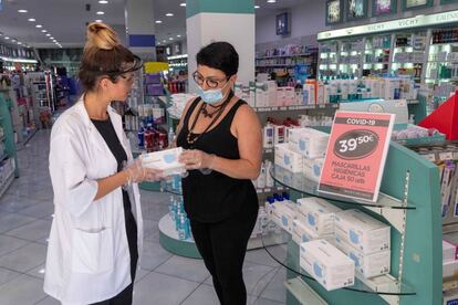 La dependienta de una tienda de cosméticos, en Murcia, enseña una caja de mascarillas a una clienta.