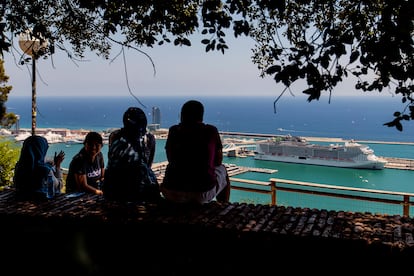 Varias personas conversan en un mirador con un crucero al fondo, en el puerto de Barcelona.