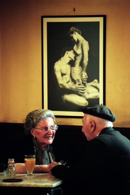 Esta fotografía cotidiana fue tomada en un pueblo del norte de Galicia llamado Viveiro en el año 1998, y surgió mientras paré a tomar un café en medio de mi labor diaria llena de prisas para un periódico para el que trabajaba entonces. Me llamó la atención la ilusión que desprendían estas personas mayores en contraste con el dibujo, que era de una exposición que exhibía el local. Me hizo pensar en lo necesario de lo cotidiano y en lo complicados que somos en eso llamado amor, y que tanto necesitamos.