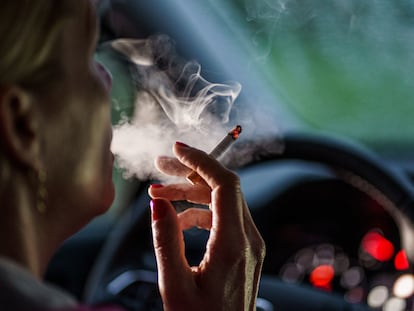 Una mujer fuma un cigarrillo dentro de un coche.