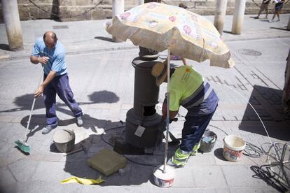 Trabajadores del Ayuntamiento de Sevilla, se protegen del sol con una sombrilla.