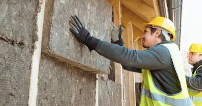 Trabajadores de la construcción colocando bloques de aislamiento ecológico en la pared exterior de una casa.