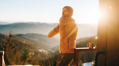 Un hombre abrochándose la chaqueta en un paraje invernal.
