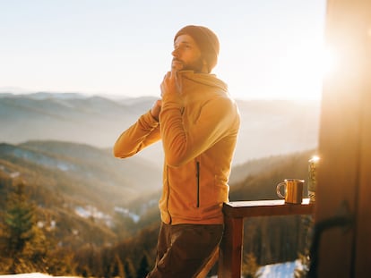 Un hombre abrochándose la chaqueta en un paraje invernal.